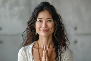A serene woman of Asian descent with curly hair poses with hands in prayer, radiating calm and tranquility. photo