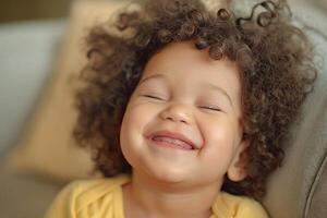 A cheerful mixed-race girl with curly hair smiles brightly, radiating joy and innocence in a cozy setting. photo