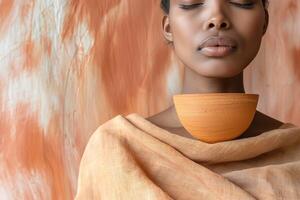 A serene Black woman with closed eyes, elegantly balancing an orange clay pot on her chest, against a warm, textured backdrop. photo