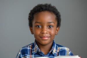 A smiling Black boy with curly hair holds a book, conveying curiosity and joy in a neutral-toned setting. photo