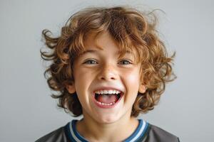 A joyful young Caucasian boy with curly hair and freckles smiles broadly against a light background. photo