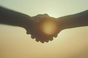 Two hands reaching out to shake, symbolizing unity and agreement against a soft sunset backdrop. photo