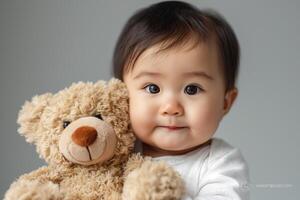 Adorable Asian baby with big expressive eyes cuddling a soft teddy bear. photo