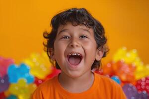 Happy young boy with curly hair, laughing joyfully against a bright orange background filled with colorful balloons. photo