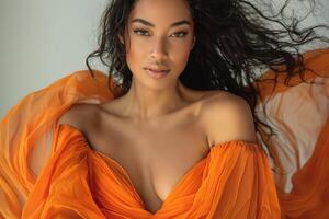 Stunning woman with long, wavy hair wearing a flowing orange dress, exuding confidence and grace. photo