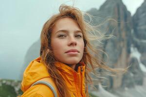 A young Caucasian woman in a vibrant yellow jacket gazes into the distance, surrounded by breathtaking mountain scenery. photo