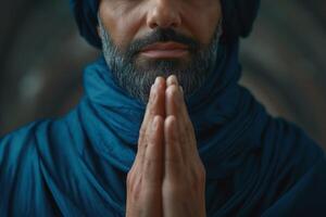 A Middle-Eastern man in traditional attire, with a thoughtful expression, prays with clasped hands against an artistic backdrop. photo
