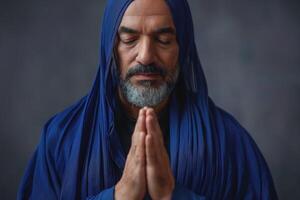 A contemplative middle-aged man of Middle Eastern descent, draped in a deep blue shawl, prays with a serene expression. photo