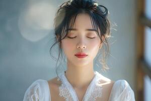 A serene young Asian woman with closed eyes, embodying tranquility in a soft-lit setting. photo
