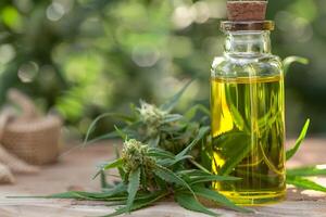 Glass Bottle with CBD Oil and Fresh Cannabis Leaves on Table photo