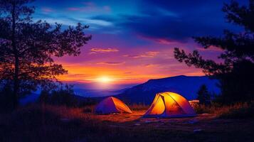 Camping under a vibrant twilight sky, two tents glow with warm light against a backdrop of majestic mountains and colorful sunset. photo