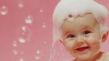 A happy baby with a mountain of foamy soap bubbles on their head smiles in a pink-toned bath, enjoying bath time with floating bubbles. photo