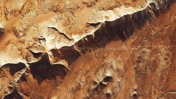 Aerial view of a rugged, sun-drenched canyon landscape featuring deep shadows, exposed rock, and dramatic geological formations. photo