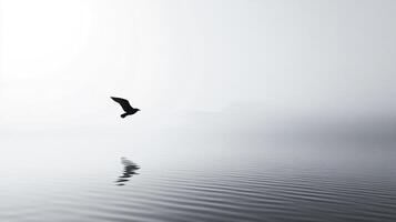 A lone bird soars over calm water in a grayscale composition, with mountain silhouettes in the background and its reflection below. photo