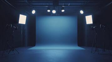 A photography studio with two cameras on tripods facing a solid, blue-grey backdrop. Overhead studio lighting is fixed to a dark ceiling. photo