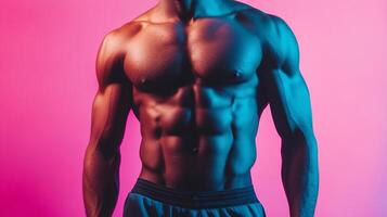 Torso of a muscular man with well-defined abdominal muscles and chest, posed in a studio setting against a vibrant pink and blue background. photo