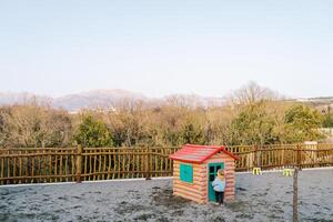 Little girl stands in front of the door of a toy house in the playground photo