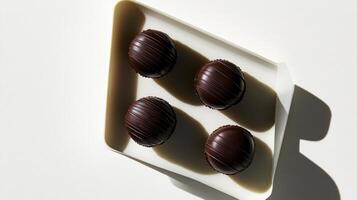 Four chocolate covered balls sit on a white plate photo