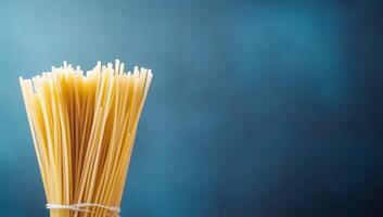 A bundle of uncooked spaghetti against a soft blue background. photo