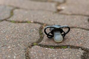 Black pacifier dropped on pavement near grass during a calm afternoon in an urban park setting photo