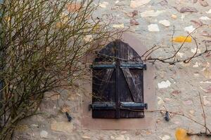 Wooden shutters adorn a rustic stone wall with bare branches in a quaint village setting during winter photo
