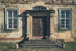 Abandoned building with weathered door and barred windows in a rural setting during daylight photo