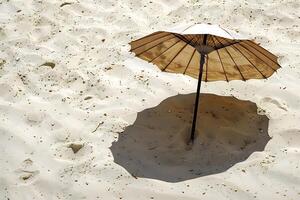 A serene beach scene featuring a weathered umbrella embedded in the sand casting a soft shadow cre photo