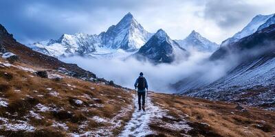A man is walking up a mountain trail with snow covered mountains in the background photo