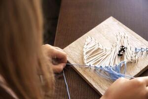 Child weaving string art on wood. Developing patience, creativity, and fine motor skills through crafting photo