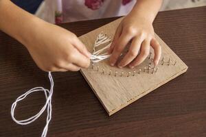 Child hands creating string art on wood. Developing fine motor skills, patience, and creativity photo