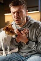 Sick man sitting on sofa at home, coughing, suffering from chest pain and respiratory issues, Symptoms of flu, asthma, or bronchitis. Illness, infection, and sickness concept photo