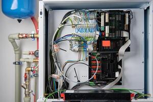 Close-up of boiler control panel with exposed electrical wiring, circuit board, and terminal connections. Modern heating system with complex electronic components photo