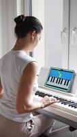 Close up view of young woman learning to play the keyboard at home using an interactive app. Using mobile apps for self-study concept. Vertical . video