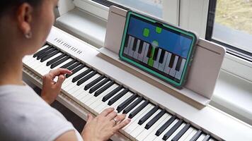 Close up view of young woman learning to play the keyboard at home using an interactive app. Using mobile apps for self-study concept. video