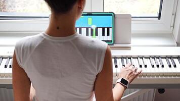 Back view of young woman learning to play the keyboard at home using an interactive app. Using mobile apps for self-study concept. video