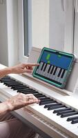 Hands playing a keyboard while following an interactive learning app on a tablet. Technology enables self-education in music without traditional lessons. Vertical . video
