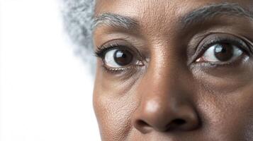 Focused gaze of an older woman, with details around the eyes and textured skin, against a plain, bright backdrop. photo