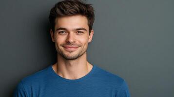 A smiling man with brown hair and a blue shirt, posing against a dark background. He is looking directly at the camera with a relaxed expression. photo
