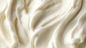 An overhead close-up shot of rich, creamy white frosting. The texture is smooth and glossy, with swirling patterns catching the light. photo