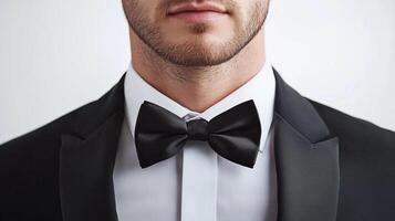 Elegant man in a black tuxedo, focusing on the crisp white shirt and satin bow tie. Ready for a formal event with style. photo