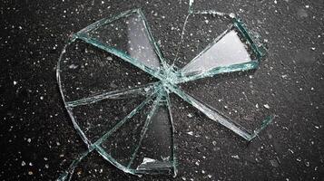 Shattered glass on dark pavement creates a radial pattern with sharp edges. Reflection catches light adding danger to this common accident. photo