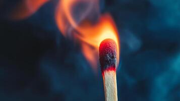 A burning matchstick captured against a dark background, showcasing the flame's bright orange and red hues with wisps of smoke. photo