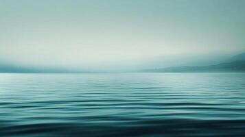 Serene turquoise landscape. Soft, misty mountains loom distantly over calm water rippling in the foreground. Quiet, peaceful, and scenic. photo