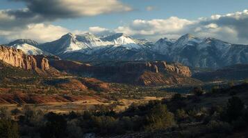 Picturesque landscape featuring snow-capped mountains, red rock formations, and lush valleys under a partly cloudy sky with perfect exposure. photo
