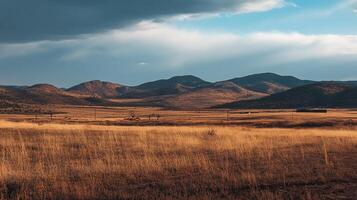 Serene landscape featuring golden grassland contrasted against a backdrop of gentle, rolling hills under a partly cloudy sky. photo
