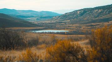 Scenic landscape featuring a tranquil lake nestled among rolling hills and autumnal grasslands, set under a soft, overcast sky. photo