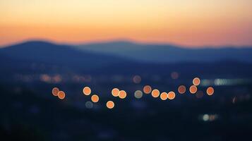 Distant city lights glow against a backdrop of mountains silhouetted by a colorful sunset, creating a dreamy and atmospheric scene. photo