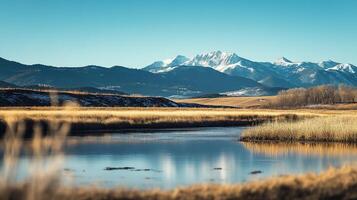Picturesque mountain scenery featuring serene lake, golden grass, and snow-capped peaks under a clear blue sky. Peaceful and tranquil. photo
