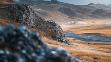Rugged rock formation amidst a vast, open valley with dry, golden grasslands and distant mountains under a soft, muted sky. photo