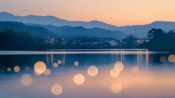 Still lake reflects the twilight sky, with soft bokeh lights dancing on the water's surface and mountains framing the horizon. photo